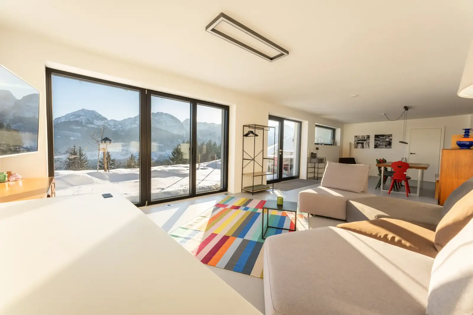 Wohnbereich mit großen Fenstern, Sofa und buntem Teppich